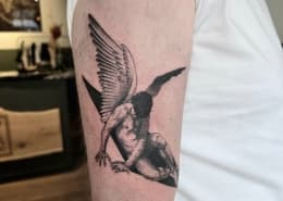 Zwart-wit tattoo van een gevallen engel op de bovenarm.