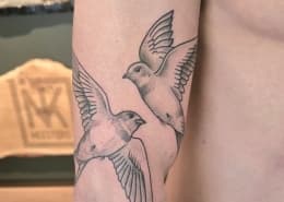 Twee vliegende zwaluwen in fineline en dotwork op de bovenarm.