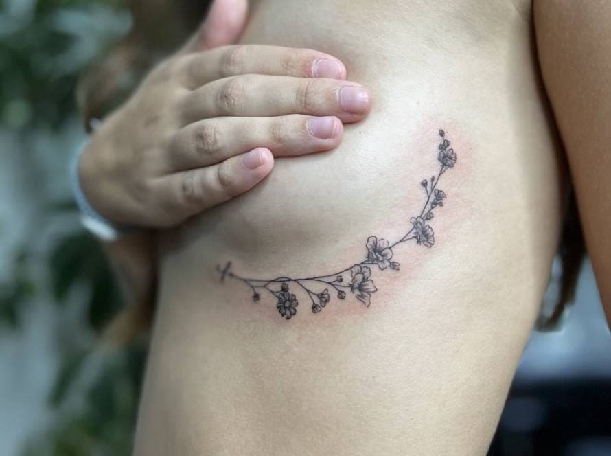 Fineline bloementak tattoo op de ribben.