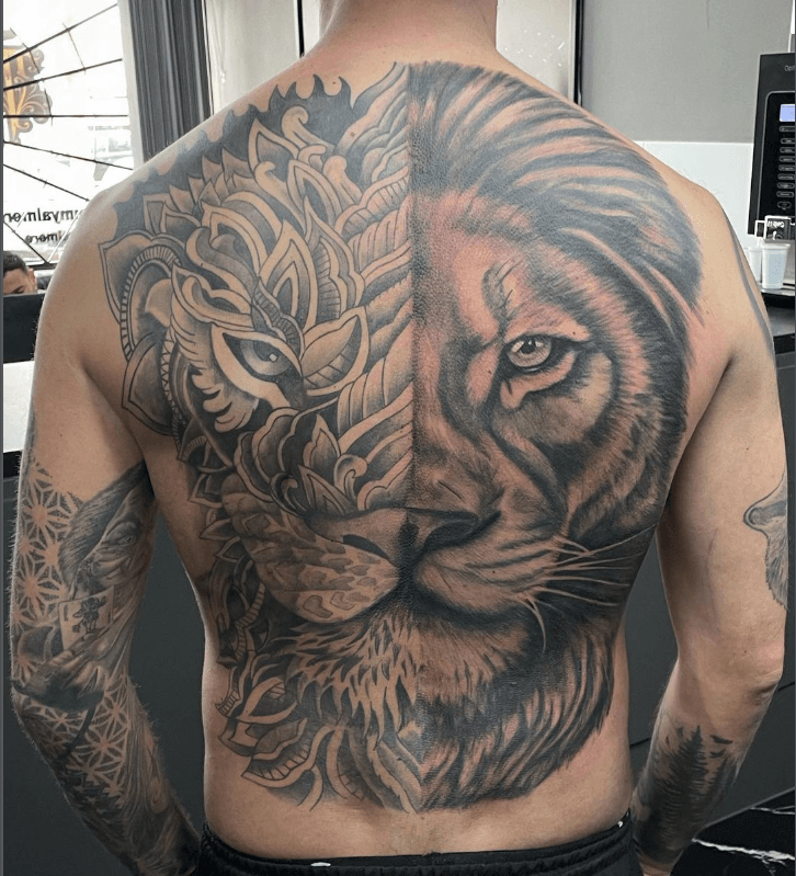 Grote rugtattoo van een leeuwenkop, half realistisch, half mandala/ornamenteel.