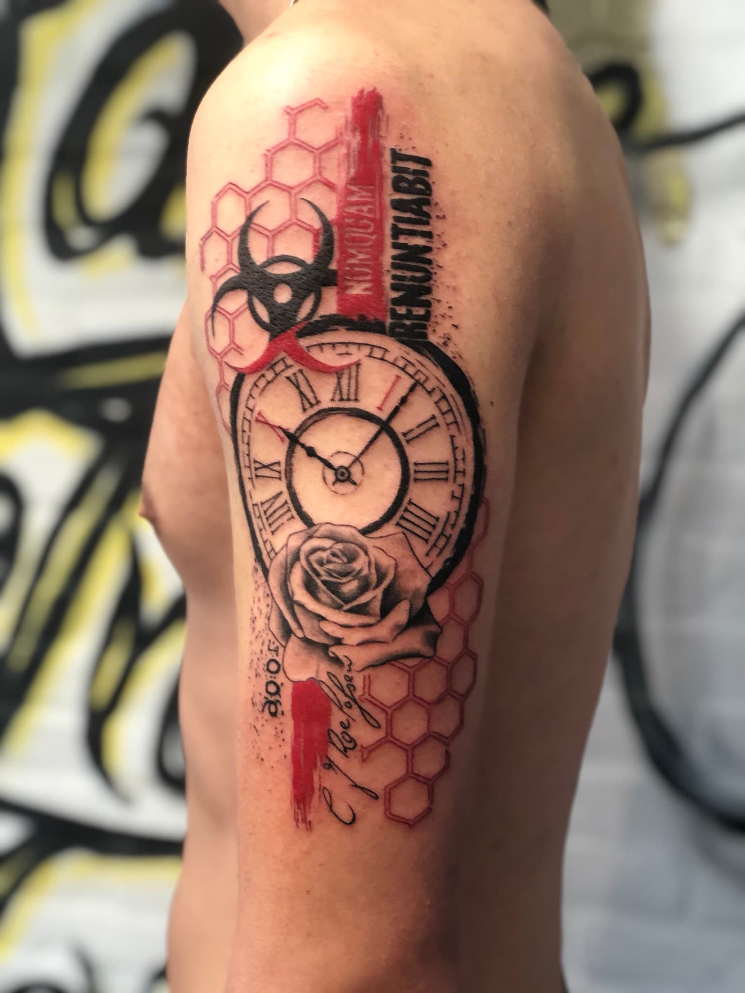 Trash polka tattoo met klok, roos, biohazard en tekst op bovenarm.