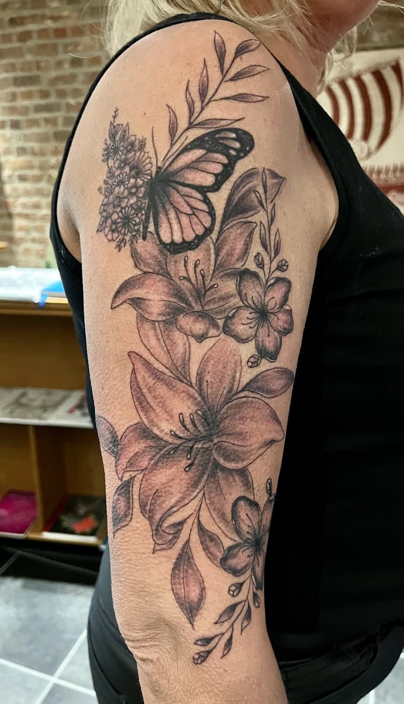 Zwart-wit bloemen en vlinder tattoo op bovenarm.