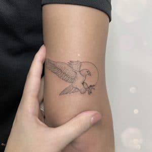 Fineline tattoo van een adelaar met een cirkel op de bovenarm.
