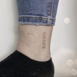Minimalistische 'BLESSED' tekst tattoo op de enkel.