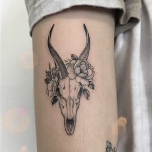 Fineline tattoo van een antilope schedel met bloemen op de bovenarm.
