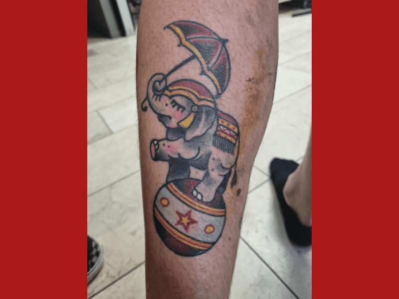 Traditionele tattoo van een circusolifant op een bal met een paraplu.