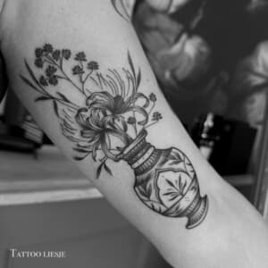 Zwart-wit tattoo van een vaas met bloemen op de bovenarm.