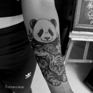 Zwart-wit tattoo van panda, schildpad en tijgerwelp op onderarm.