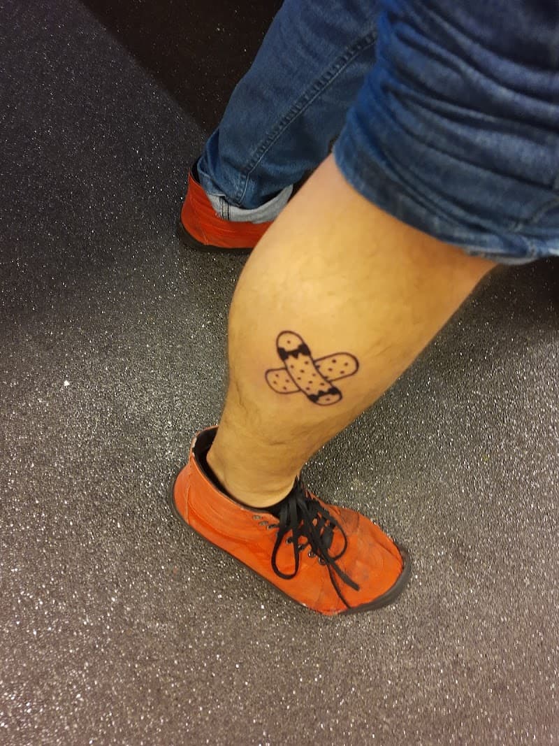Illustratieve tattoo van twee gekruiste pleisters op het onderbeen.