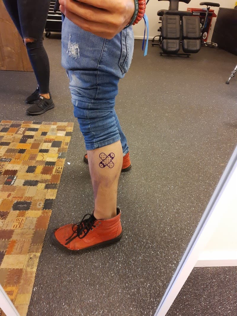 Kleine paarse tattoo van gekruiste pleisters op onderbeen.