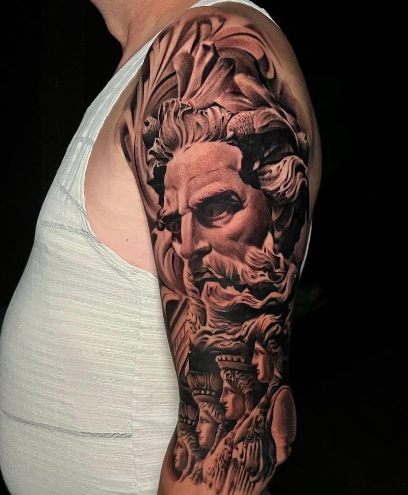 Realistische zwart-wit tattoo van een Grieks standbeeld (Zeus/Poseidon) op de bovenarm.