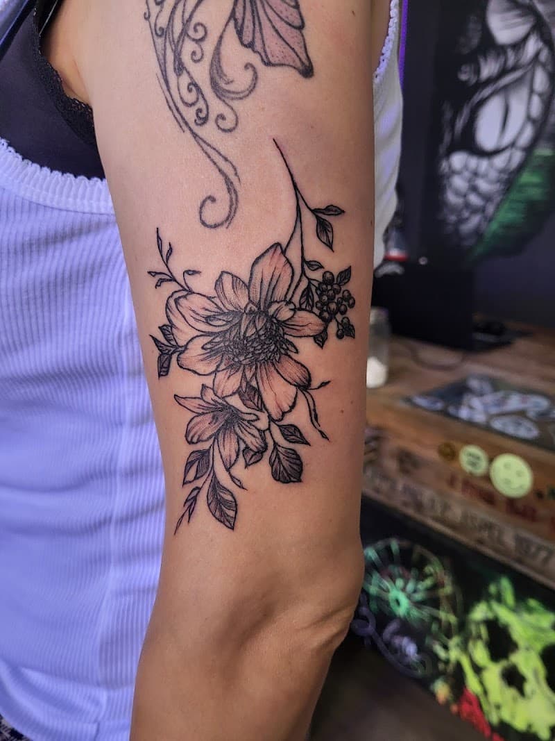 Fineline bloemen tattoo met bladeren en bessen op bovenarm.