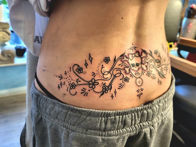 Fineline onderrug tattoo van een schedel met strik en sierlijke ornamenten.