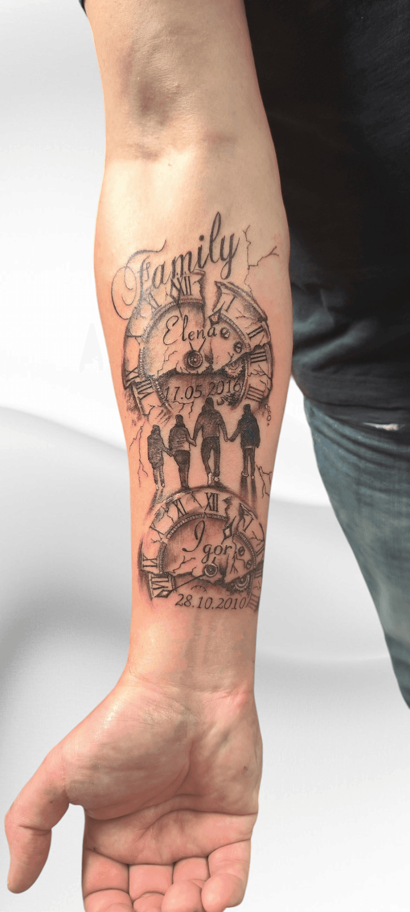 Zwart-wit tattoo op onderarm met twee klokken, namen Elena en Igor, datums en een gezin.