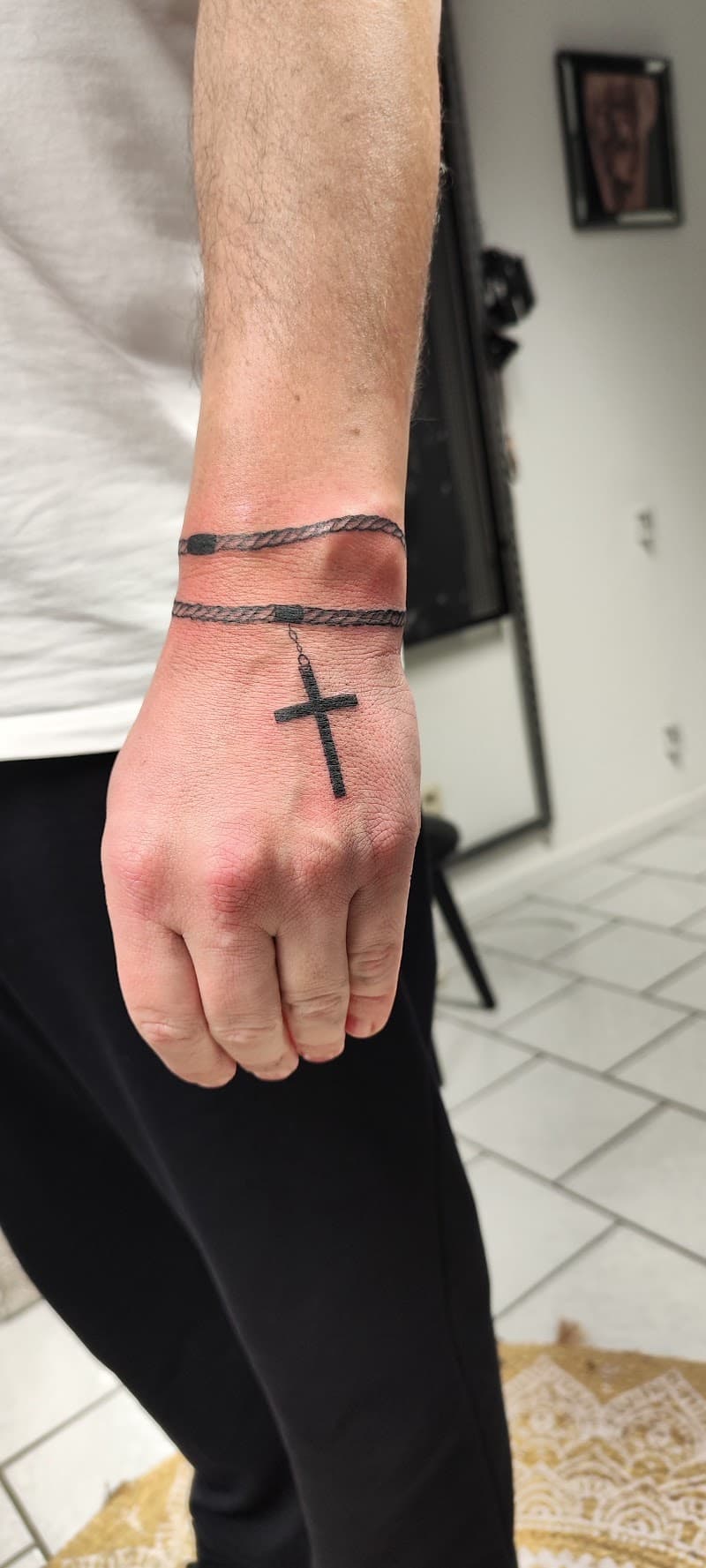 Minimalistische rozenkrans tattoo met kruisje op hand en pols.