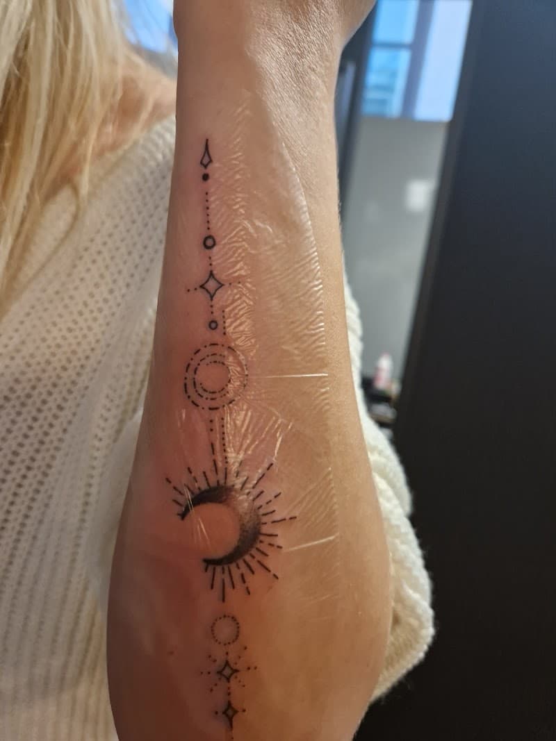 Fineline tattoo van maan, zon en geometrische vormen op onderarm.