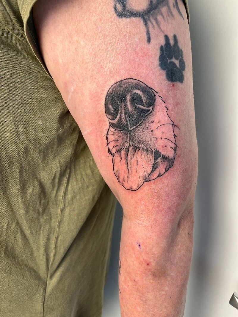 Gedetailleerde blackwork tattoo van een hondenneus en tong op de bovenarm.