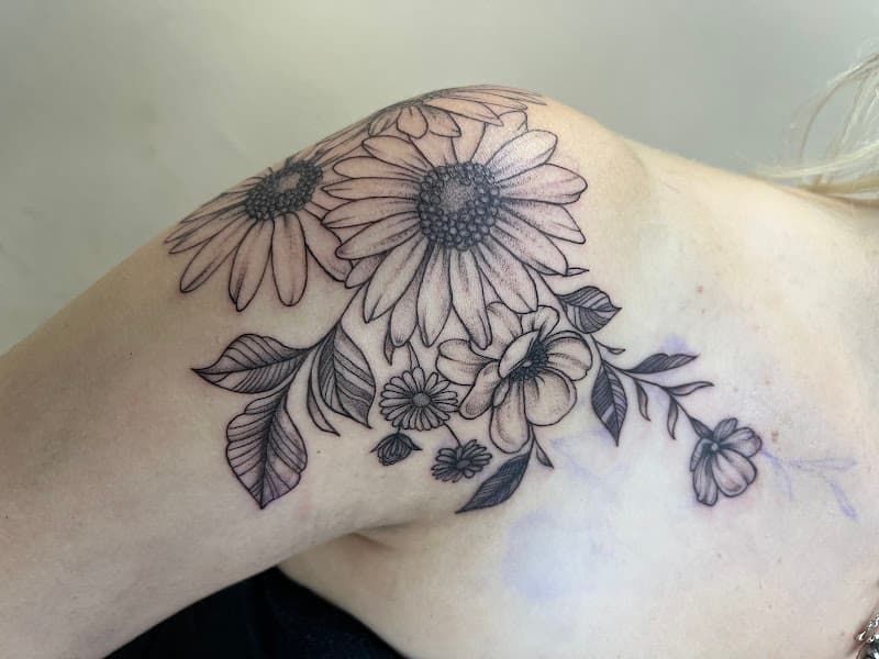 Grote fineline bloemen tattoo op schouder met madeliefjes en bladeren.
