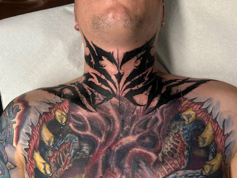 Zwarte abstracte 'tribal' nek tattoo boven een gekleurd borststuk.