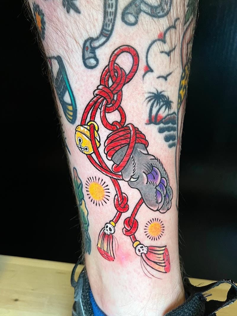 Traditionele tattoo van een dierenpoot met rood touw en bellen op onderbeen.