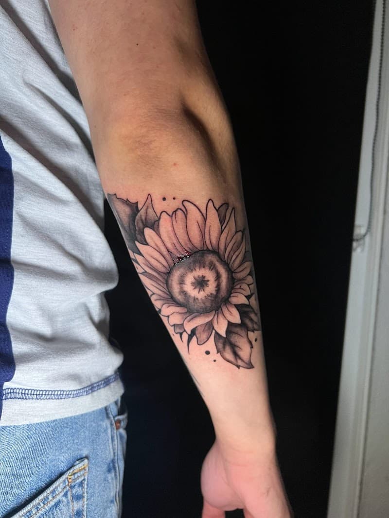 Zwart-wit zonnebloem tattoo op de onderarm met bladeren en dotwork.