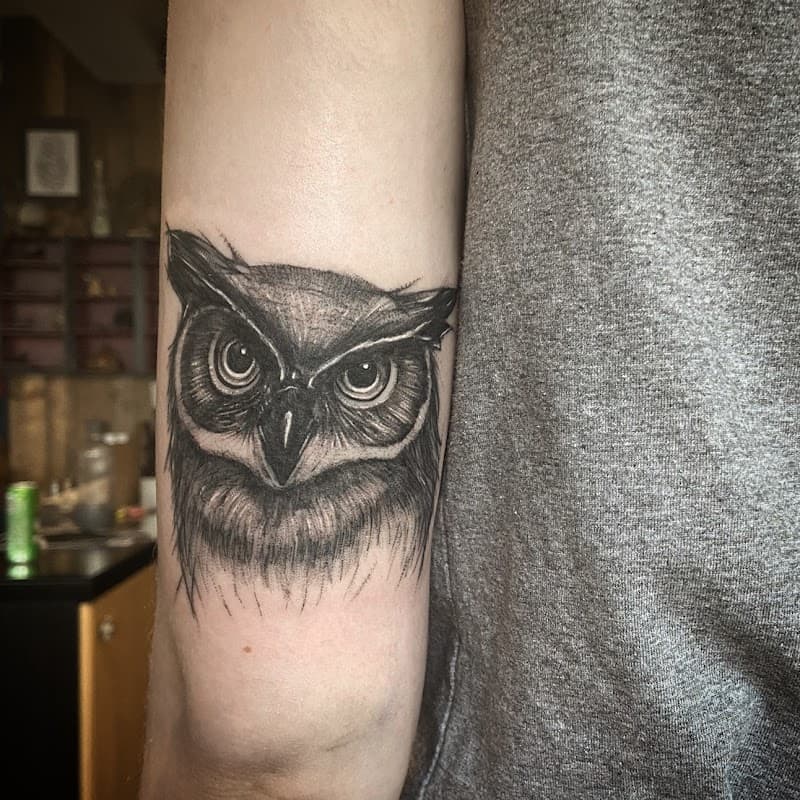 Gedetailleerde zwart-wit uilenkop tattoo op de bovenarm.