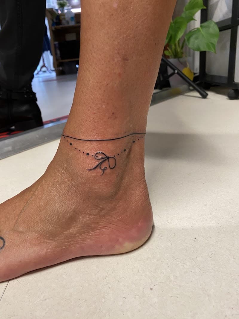 Fijne lijn enkelband tattoo met een klein strikje en stippen.