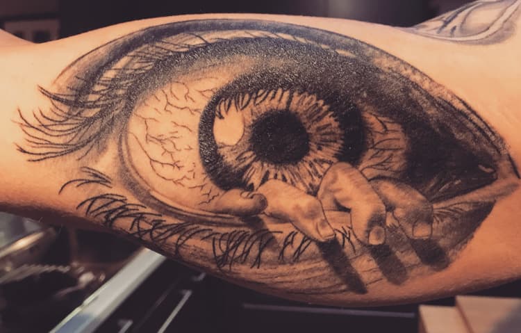 Realistisch oog met hand die eruit komt op bovenarm.