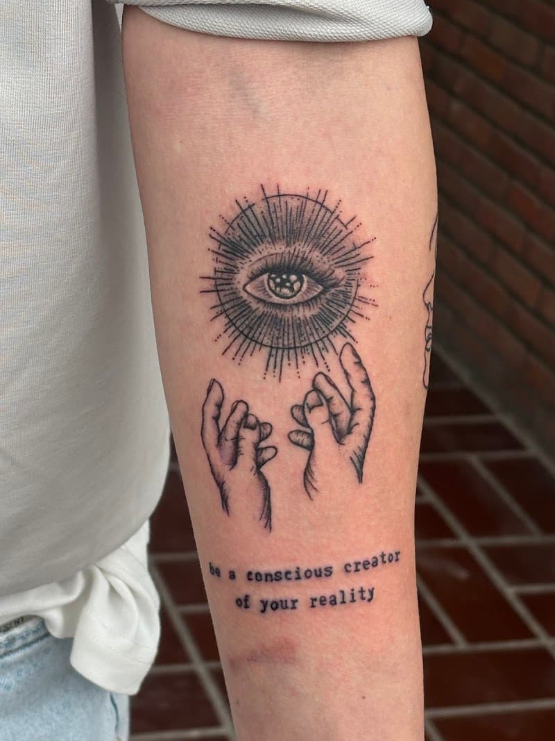 Zwart-wit tattoo van een oog met stralen, twee handen en tekst op de onderarm.