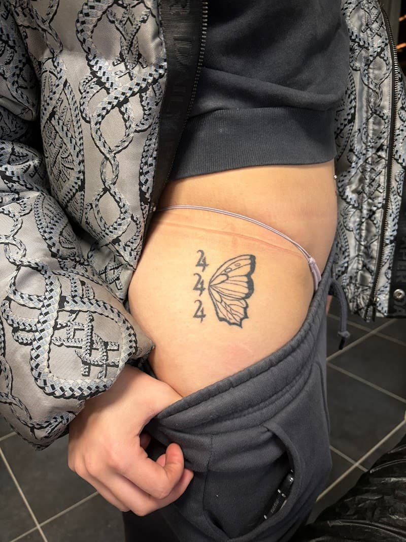 Zwart-wit tattoo van het getal 444 en een halve vlinder op de heup.