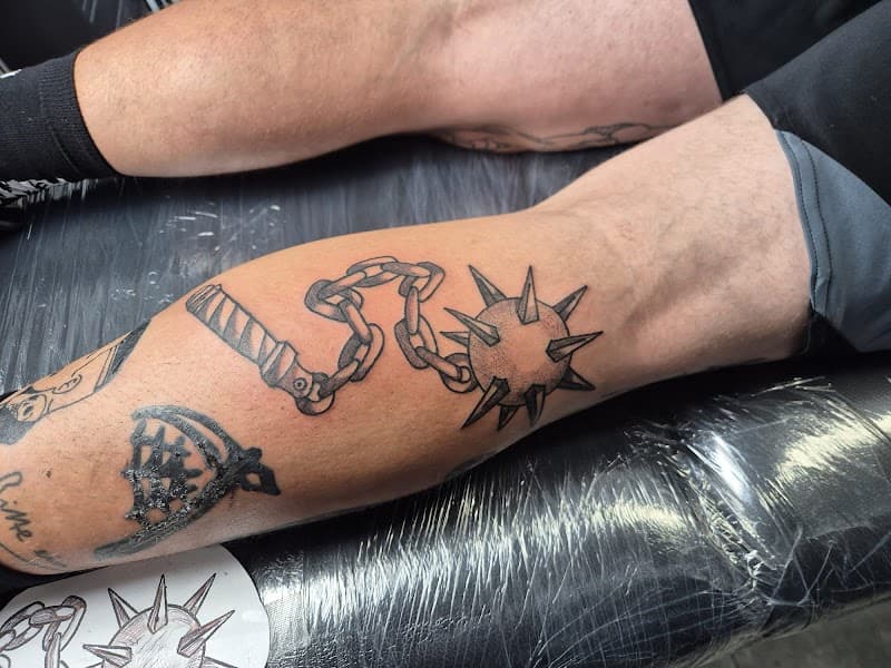 Zwart-wit tattoo van een morgenster (vlegel) met ketting op het onderbeen.