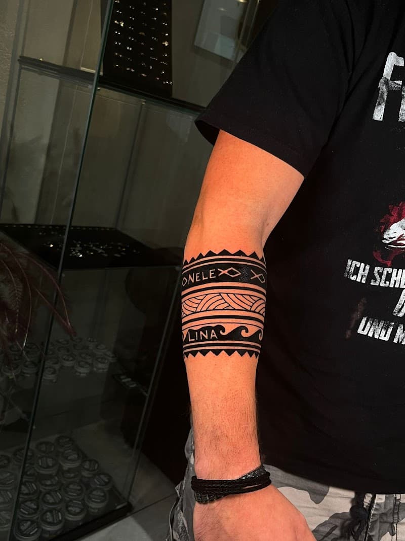 Zwarte tribal band tattoo met namen ONELE en LINA op onderarm.