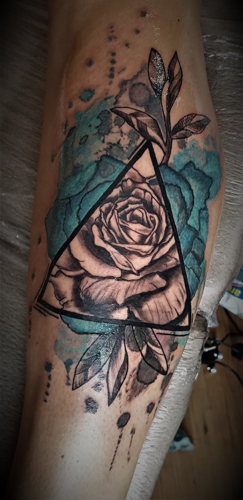 Roos in driehoek met blauwe watercolor spetters op onderbeen.