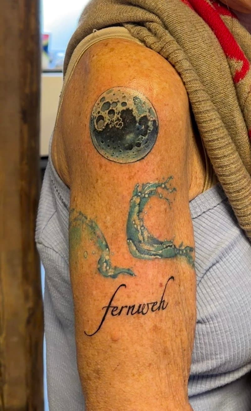 Gedetailleerde maan, watergolf en 'fernweh' tekst op bovenarm.