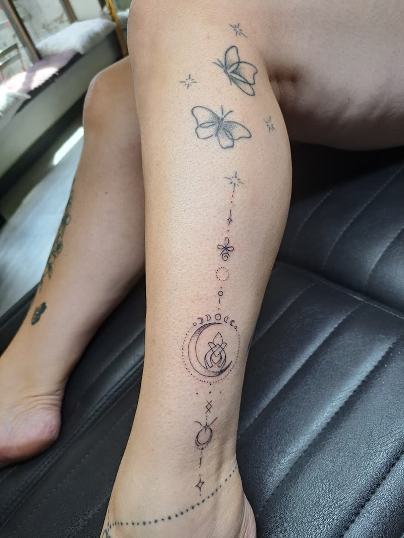 Fineline tattoo met vlinders, maan, sterren en symbolen op onderbeen.