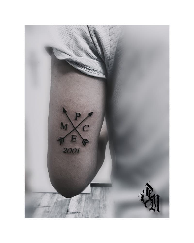 Minimalistische tattoo met gekruiste pijlen, letters M P C E en jaartal 2001.