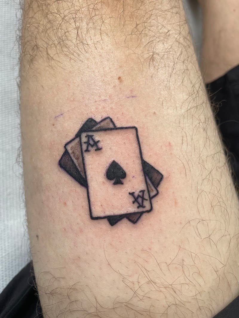 Kleine tattoo van drie speelkaarten, met de schoppenaas bovenop.