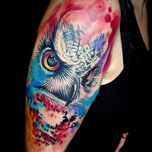 Kleurrijke uil tattoo in watercolor stijl op de bovenarm.
