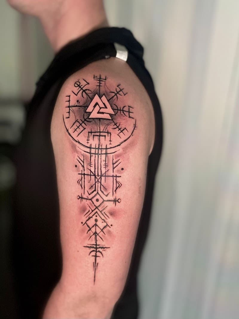 Blackwork tattoo op bovenarm met Valknut, runenkompas en geometrische patronen.