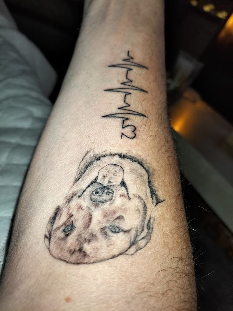 Twee tattoos op onderarm: hartslag met nummer 3 en een hondenportret.