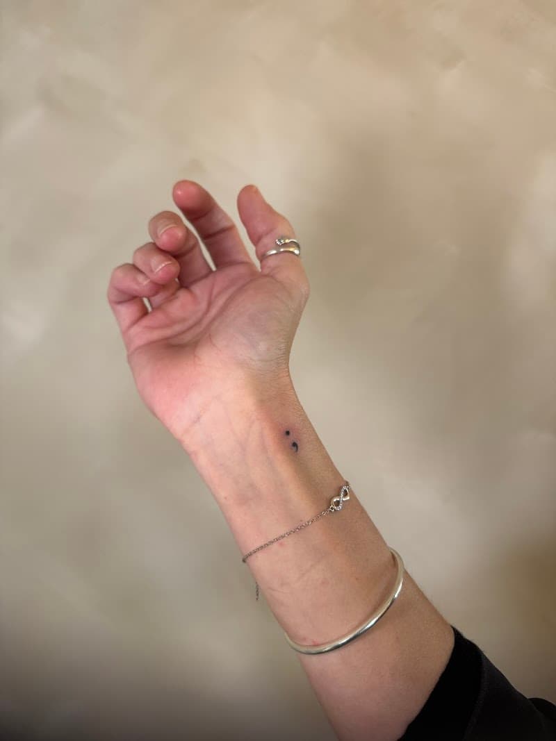 Kleine minimalistische puntkomma tattoo op de pols.