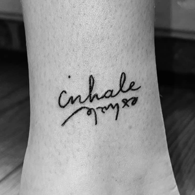Sierlijke 'inhale exhale' tekst tattoo op de enkel.