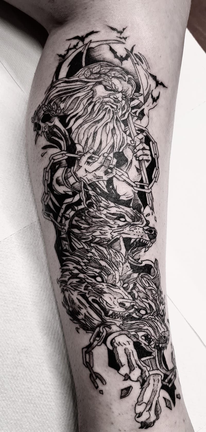 Illustratieve tattoo van een oude man met kettingen en drie wolvenkoppen op het onderbeen.