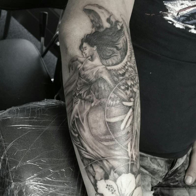 Zwart-wit tattoo van een engel met vleugels op de onderarm.