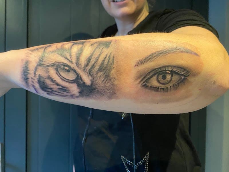Realistische tattoo van een tijgeroog en een mensenoog op de onderarm.