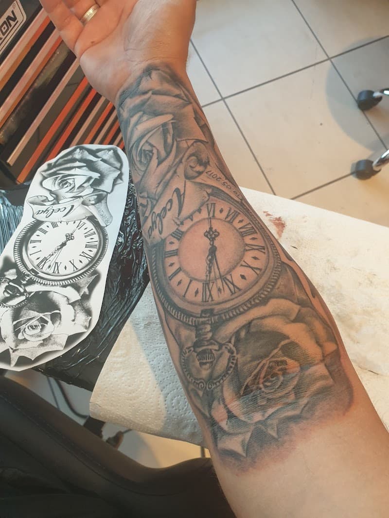 Realistische zwart-wit tattoo van een zakhorloge, twee rozen en een naam op de onderarm.