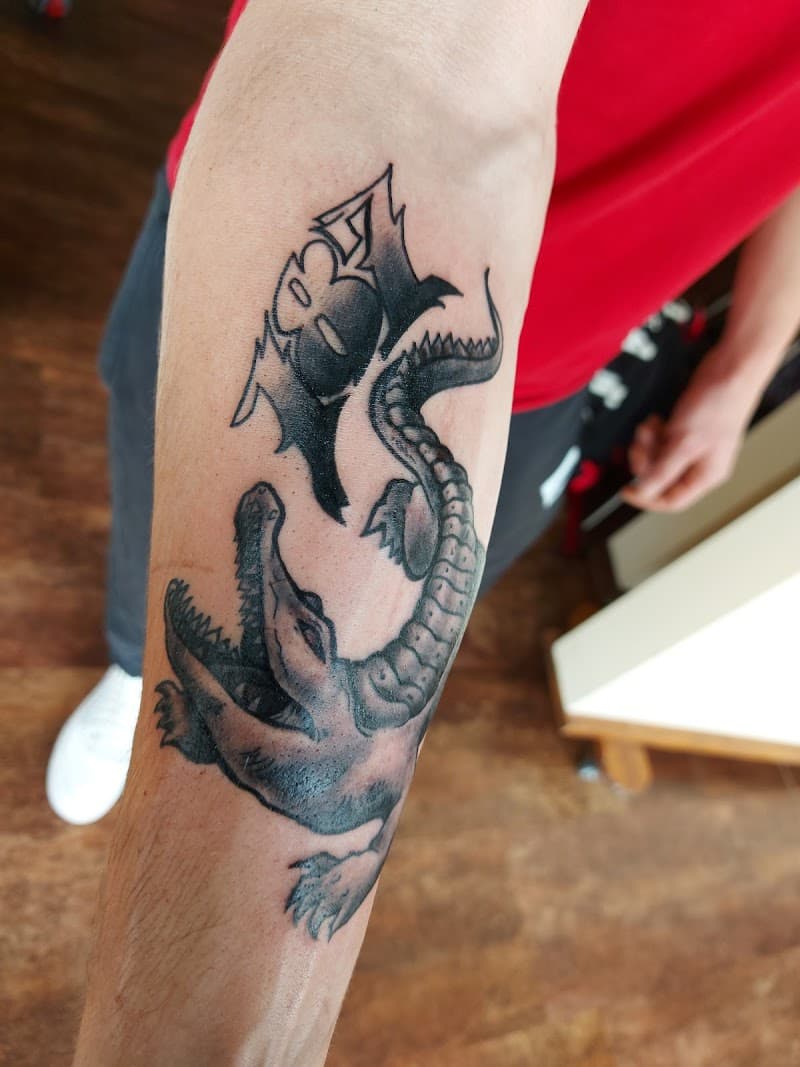 Blackwork krokodil met een gestileerd symbool erboven op de onderarm.