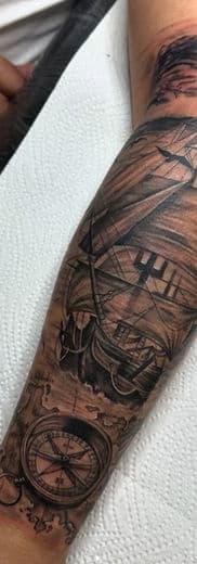 Zwart-wit tattoo van een zeilschip en kompas op een onderarm.