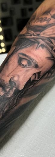 Realistisch portret van Jezus met doornenkroon op een bovenarm.