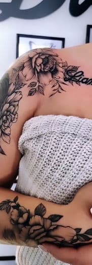 Zwart-grijze bloemen tattoos op schouder, bovenarm en onderarm met naam.